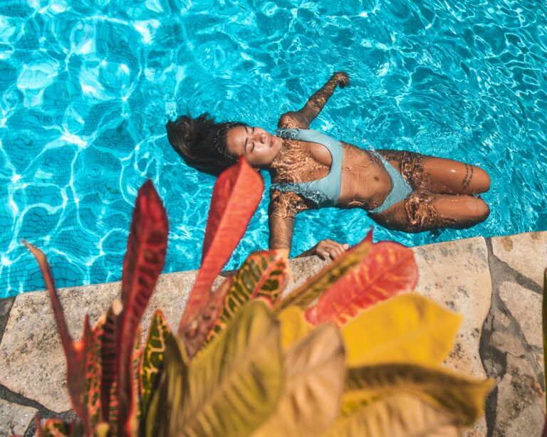 A serene image of an Asian woman relaxing in a swimming pool, surrounded by sunny reflections and vibrant plants.